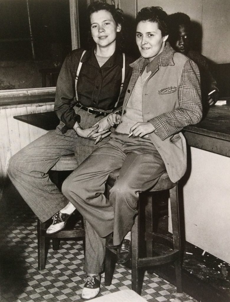 A black and white photo - a couple sits on barstools.