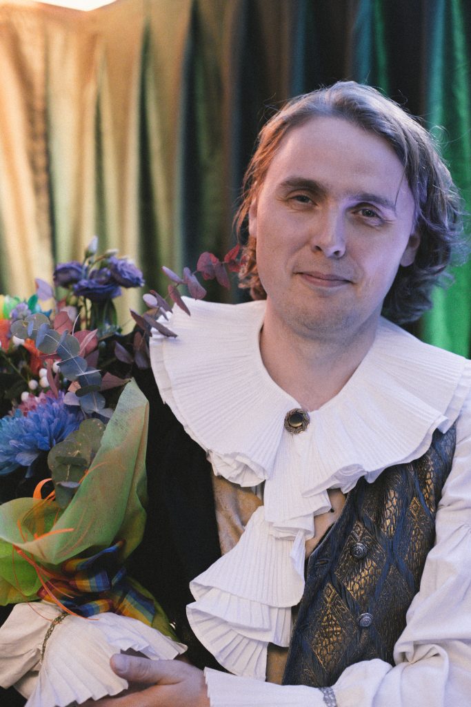A person in Shakespear inspired clothes, holding flowers.